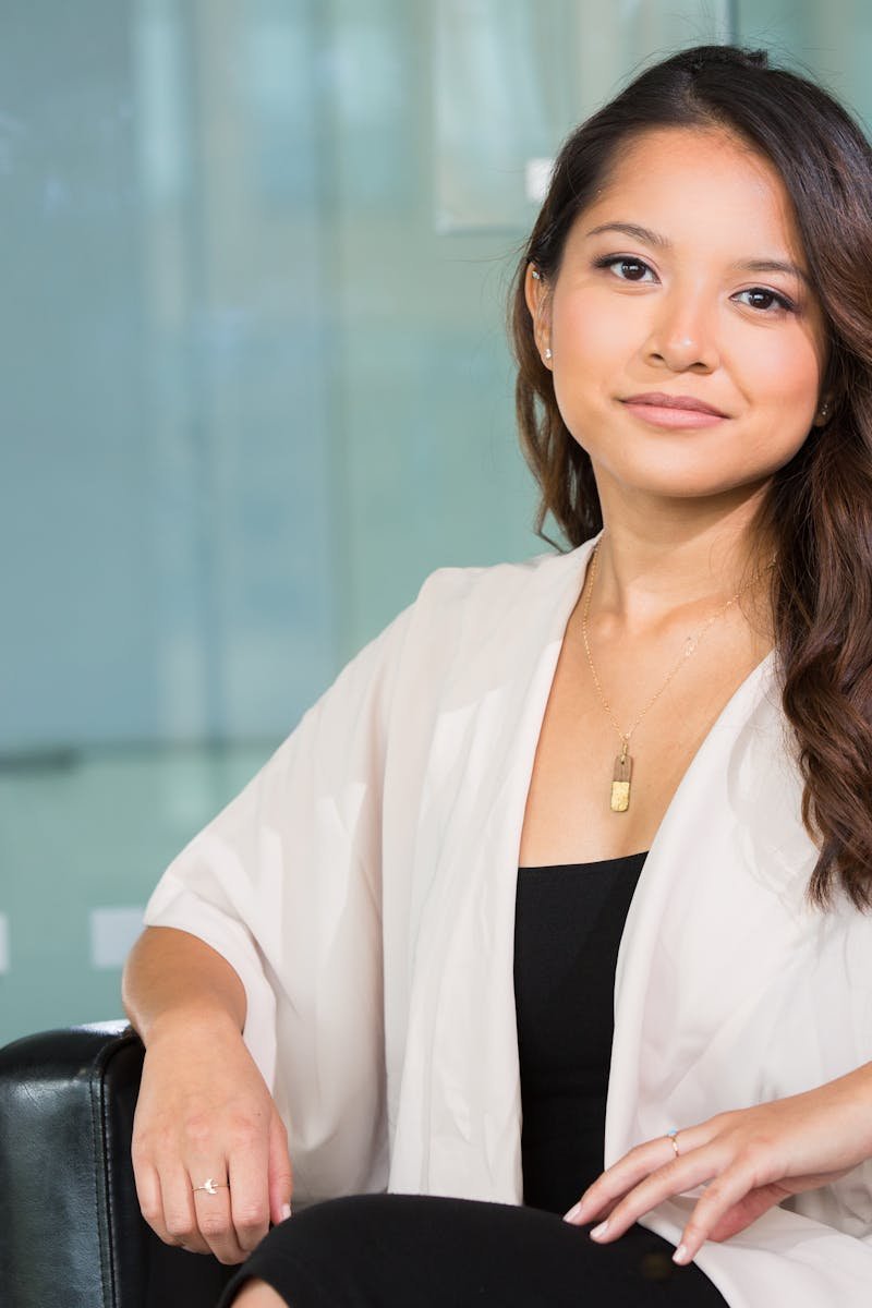 A professional Asian businesswoman sitting confidently in a modern office setting.